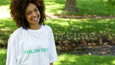 漂亮的志愿者对着镜头微笑，指着T恤